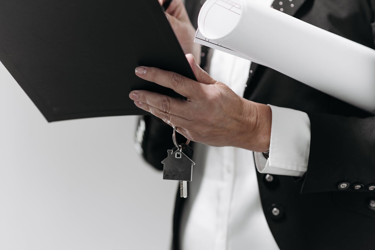 Close-up of a business professional holding a house key and architectural plans, symbolizing real estate.